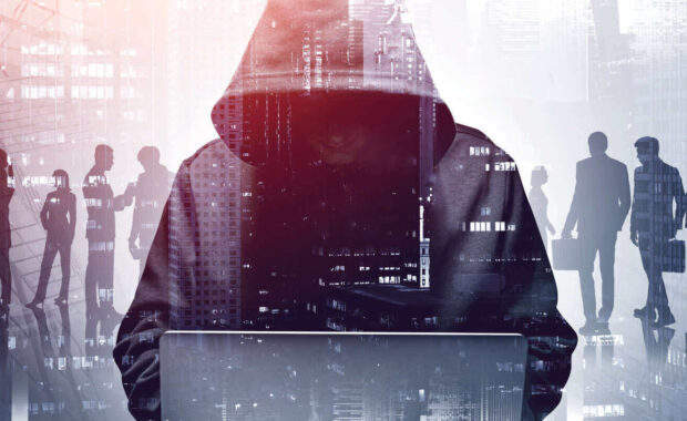 young hacker in hoodie using laptop in blurry city